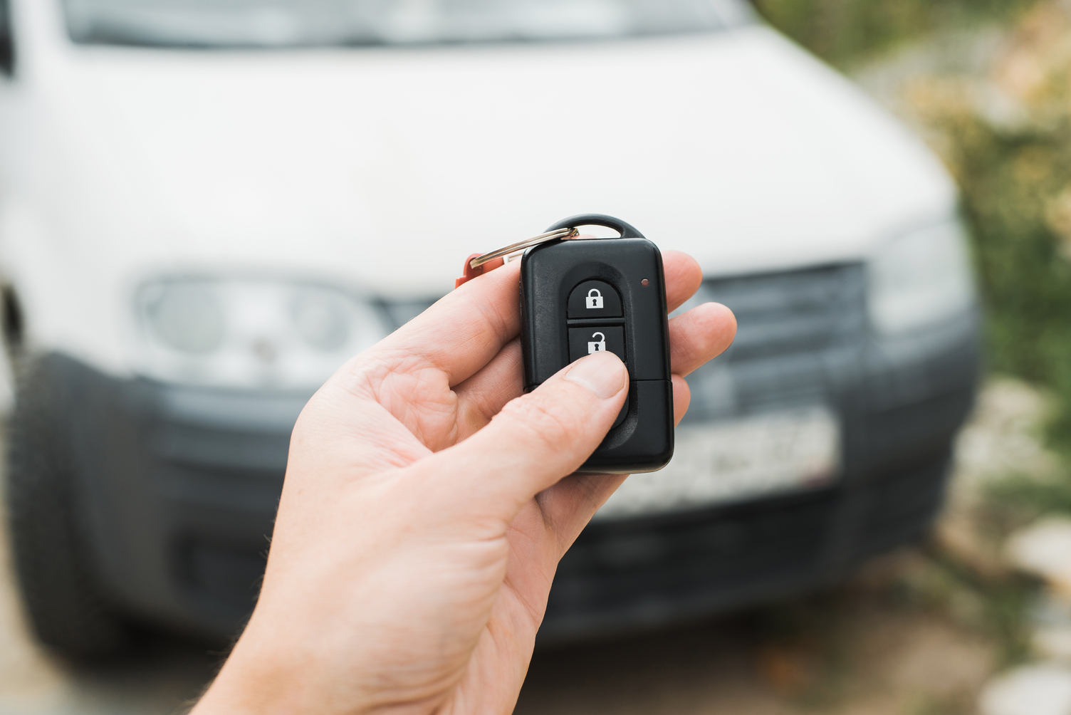 Mano sosteniendo un mando a distancia de coche con un vehículo en el fondo.