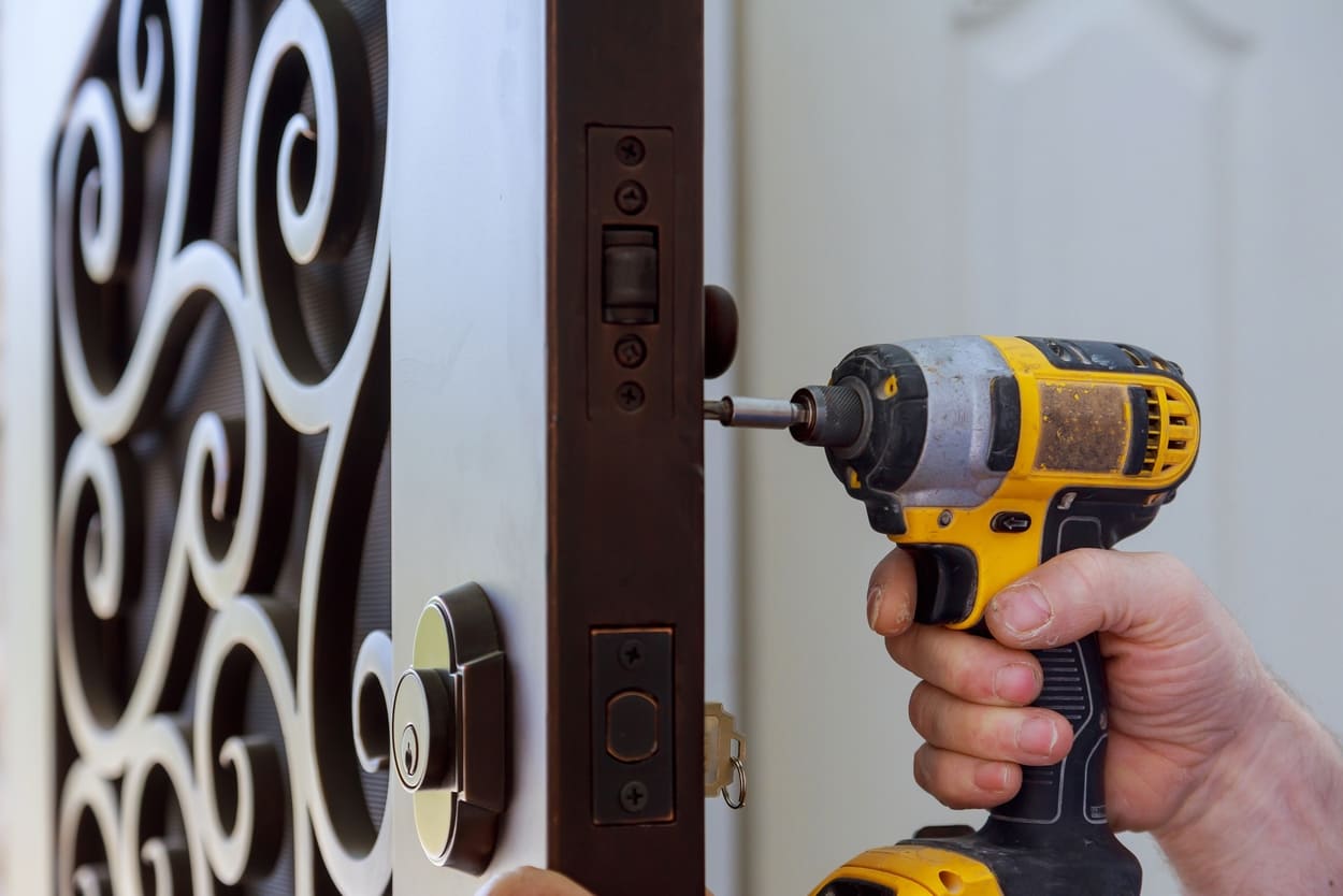 Mano utilizando un taladro eléctrico para instalar una cerradura en una puerta.